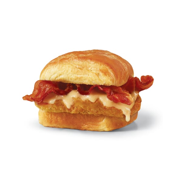 Crispy chicken sandwich with bacon and melted cheese on a toasted bun, isolated on white.